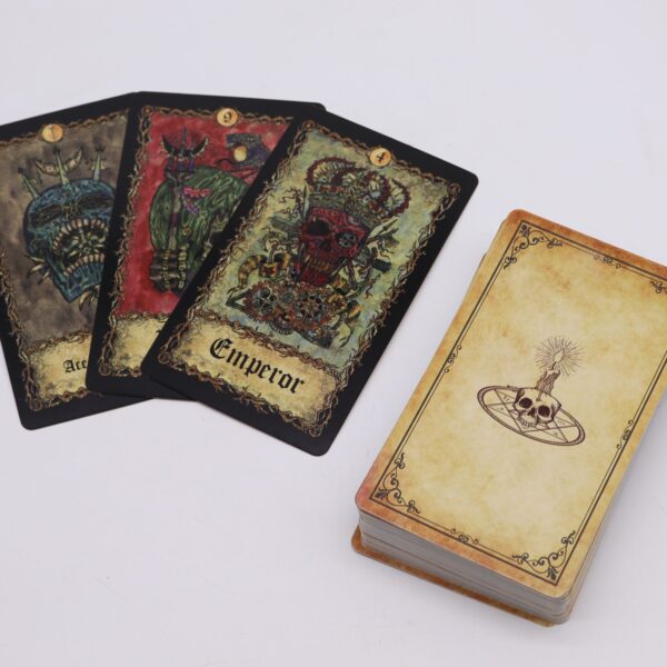 Cartas de tarot gótico con calaveras ilustradas, el Emperador con corona, y mazo con reverso color pergamino