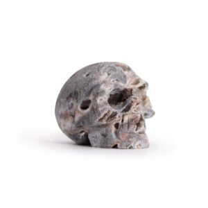 Calavera pequeña tallada en geoda de calcita gris y rosada, vista de perfil