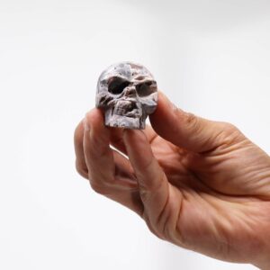 Calavera pequeña tallada en geoda de calcita gris y rosada, vista de perfil