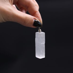 Colgante de selenita blanca en bruto con forma de barra rectangular y estrías verticales, con anilla metálica arriba, sobre fondo blanco