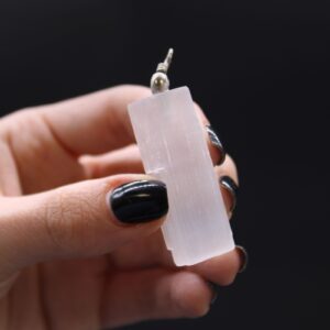 Colgante de selenita blanca en bruto con forma de barra rectangular y estrías verticales, con anilla metálica arriba, sobre fondo blanco