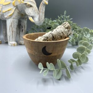 Cuenco de madera de mango con una media luna negra en el costado y un atado de salvia dentro