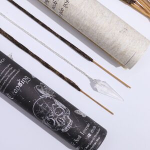 Tubo negro de incienso ritual Purificación junto a la lámina enrollada con el péndulo de cristal de roca