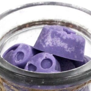 Tarro de vidrio abierto lleno de tabletas de cera de soja lilas con forma de corazón, vistas desde arriba