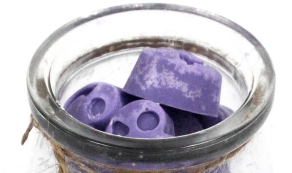 Tarro de vidrio abierto lleno de tabletas de cera de soja lilas con forma de corazón, vistas desde arriba