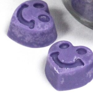 Tarro de vidrio abierto lleno de tabletas de cera de soja lilas con forma de corazón, vistas desde arriba