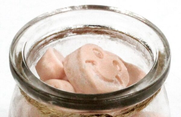 Tarro de vidrio abierto con tabletas de cera de soja rosa pálido en forma de corazón con cara sonriente