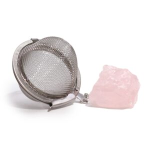 Colador de té de bola de acero inoxidable junto a un trozo de cuarzo rosa en bruto
