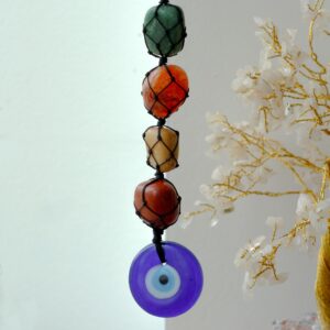Colgante decorativo de siete piedras de colores en red de cordón negro con un ojo turco azul al final, colgado de una rama blanca