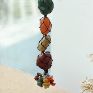 Colgante de siete piedras de los chakras en red de cordón negro con racimo de lascas de colores, colgado de una rama blanca