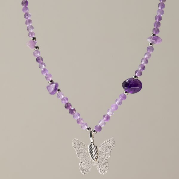 Collar de amatista lila en cuentas facetadas, con lascas violeta y una mariposa plateada formada sobre una hoja natural