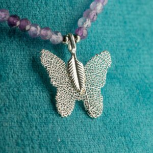 Collar de amatista lila en cuentas facetadas, con lascas violeta y una mariposa plateada formada sobre una hoja natural