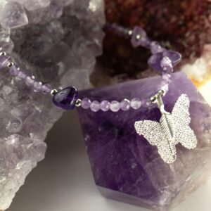 Collar de amatista lila en cuentas facetadas, con lascas violeta y una mariposa plateada formada sobre una hoja natural