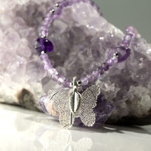 Collar de amatista lila en cuentas facetadas, con lascas violeta y una mariposa plateada formada sobre una hoja natural