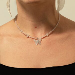 Collar de cuarzo rosa pálido en cuentas facetadas, con lascas lechosas y una mariposa metalizada sobre una hoja natural