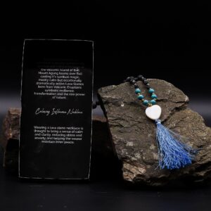 Collar largo de cuentas de piedra de lava con tramo turquesa, corazón blanco y borla azul, junto a su caja negra