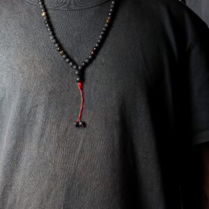 Collar largo de cuentas de piedra de lava negra y ojo de tigre con remate de cordón rojo y dos cuentas colgando, junto a su caja negra