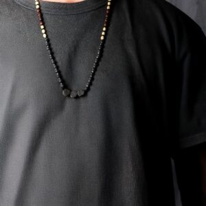Collar largo de cuentas de piedra de lava negra con tres discos volcánicos en el centro y un tramo de cuentas beige y marrones, junto a su caja