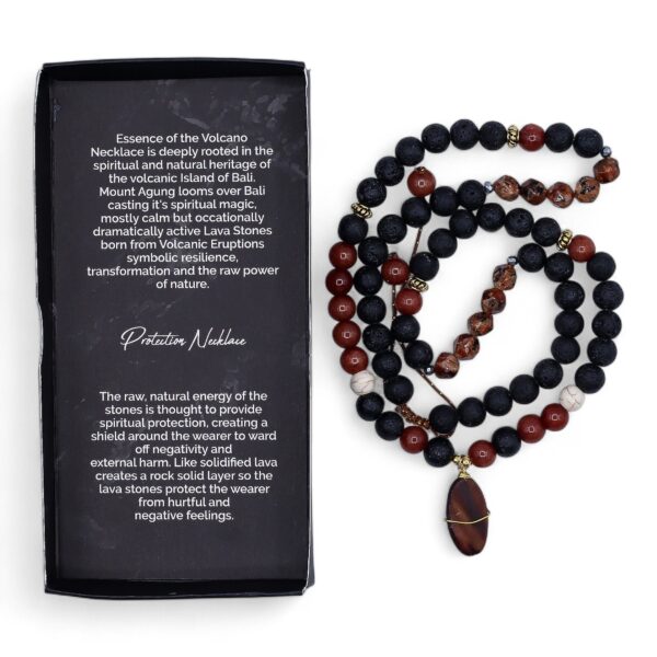 Collar largo de cuentas de lava negra y cuentas rojas con colgante ovalado de piedra rojiza envuelto en alambre dorado, junto a su caja