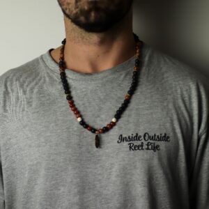 Collar largo de cuentas de lava negra y cuentas rojas con colgante ovalado de piedra rojiza envuelto en alambre dorado, junto a su caja