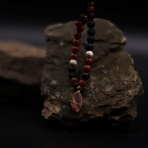 Collar largo de cuentas de lava negra y cuentas rojas con colgante ovalado de piedra rojiza envuelto en alambre dorado, junto a su caja
