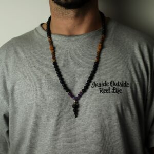 Collar de cuentas de lava negra con tramos de cuentas moradas facetadas y colgante de lava con casquillo plateado, junto a su caja negra