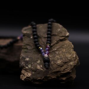 Collar de cuentas de lava negra con tramos de cuentas moradas facetadas y colgante de lava con casquillo plateado, junto a su caja negra