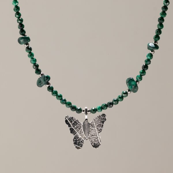 Collar de cuentas facetadas de malaquita verde con lascas pulidas y una mariposa plateada que conserva los nervios de una hoja real