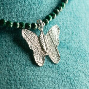 Collar de cuentas facetadas de malaquita verde con lascas pulidas y una mariposa plateada que conserva los nervios de una hoja real