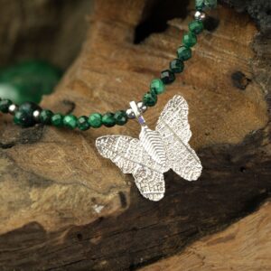 Collar de cuentas facetadas de malaquita verde con lascas pulidas y una mariposa plateada que conserva los nervios de una hoja real