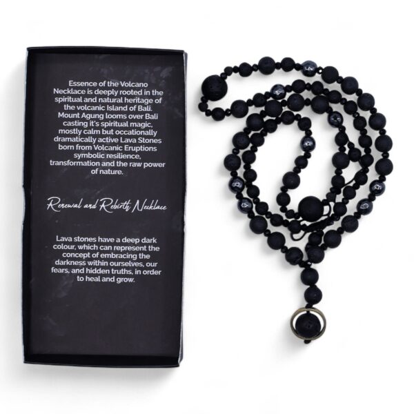 Collar negro de cuentas de piedra de lava y cuentas facetadas con colgante de una cuenta de lava dentro de un aro dorado, junto a su caja