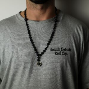 Collar negro de cuentas de piedra de lava y cuentas facetadas con colgante de una cuenta de lava dentro de un aro dorado, junto a su caja