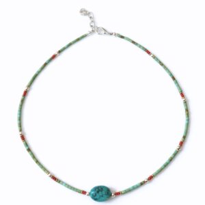 Collar fino de tubitos color turquesa verdoso con una piedra central ovalada de vetas negras y pequeños detalles rojos, plateados y dorados, sobre fondo blanco