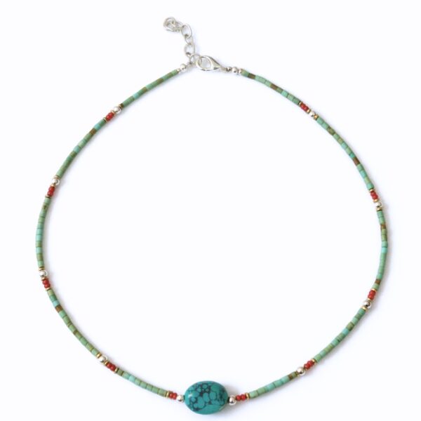 Collar fino de tubitos color turquesa verdoso con una piedra central ovalada de vetas negras y pequeños detalles rojos, plateados y dorados, sobre fondo blanco
