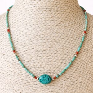 Collar fino de tubitos color turquesa verdoso con una piedra central ovalada de vetas negras y pequeños detalles rojos, plateados y dorados, sobre fondo blanco