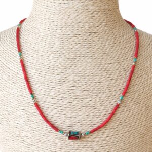 Collar fino de cuentas rojo coral con toques turquesa y una cuenta central dorada con incrustaciones, puesto en un busto de rafia