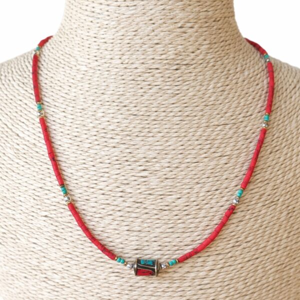 Collar fino de cuentas rojo coral con toques turquesa y una cuenta central dorada con incrustaciones, puesto en un busto de rafia