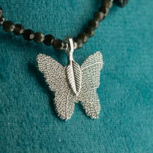 Collar negro de obsidiana facetada y lascas pulidas alrededor de una mariposa con baño de plata y nervadura de hoja