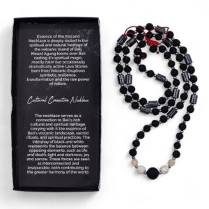 Collar largo de cuentas de piedra de lava negra y tubos grises con howlita blanca en el centro y nudo de macramé rojo, junto a su caja