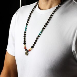 Collar de cuentas de piedra de lava con separadores dorados, cuentas turquesa y rojas y medalla redonda con el símbolo Om, junto a su caja