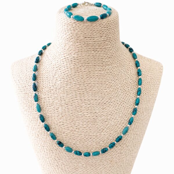 Conjunto de collar y pulsera de cuentas alargadas de howlita teñida color turquesa con vetas oscuras y bolitas plateadas, en un busto