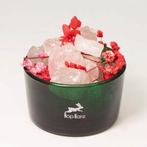 Tarro de vidrio verde con trozos de cuarzo rosa en bruto y flores secas rojas y rosas