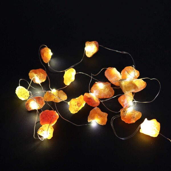 Guirnalda de luces LED encendida con piedras naranjas en bruto sobre fondo negro