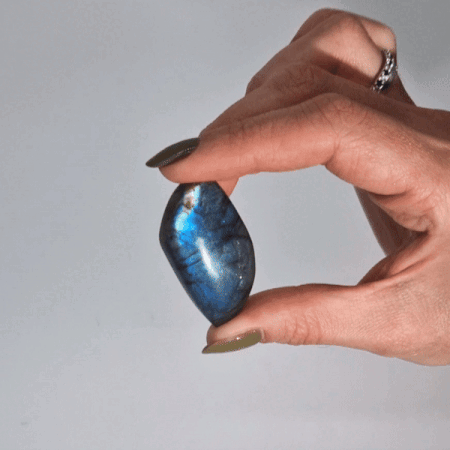 Mano sosteniendo una labradorita pulida en forma de hoja con un destello azul intenso