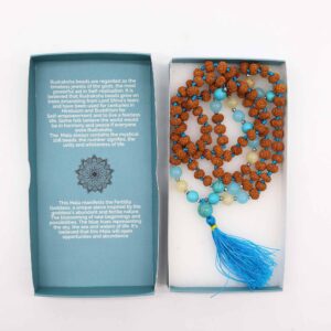 Mala de semillas de rudraksha anudado con hilo turquesa, cuentas turquesa, azul agua y amarillo pálido y borla azul, junto a su caja