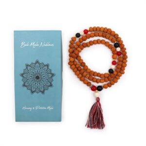 Mala de semillas de rudraksha con cuentas rojas, blancas y negras y borla tricolor, junto a su caja turquesa