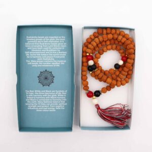 Mala de semillas de rudraksha con cuentas rojas, blancas y negras y borla tricolor, junto a su caja turquesa