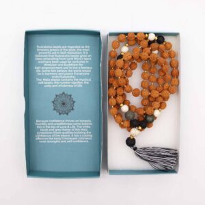 Mala largo de semillas de rudraksha con cuentas blancas, negras y grises y borla en negro y blanco, junto a su caja azul