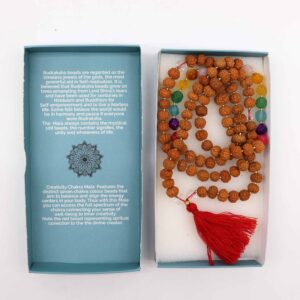 Mala de semillas de rudraksha con cuentas facetadas de los siete colores de los chakras y borla roja, junto a su caja azul