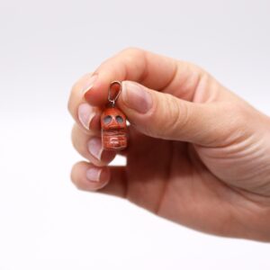 Doce colgantes de calavera tallados en piedra con asa plateada sobre una mano: amatista, cuarzo rosa, aventurina, sodalita, jaspe rojo, cristal de roca y opalita